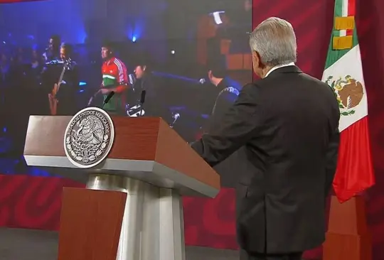 AMLO durante la conferencia de prensa mañanera mientras ve el video de América de los Tigres del Norte. 