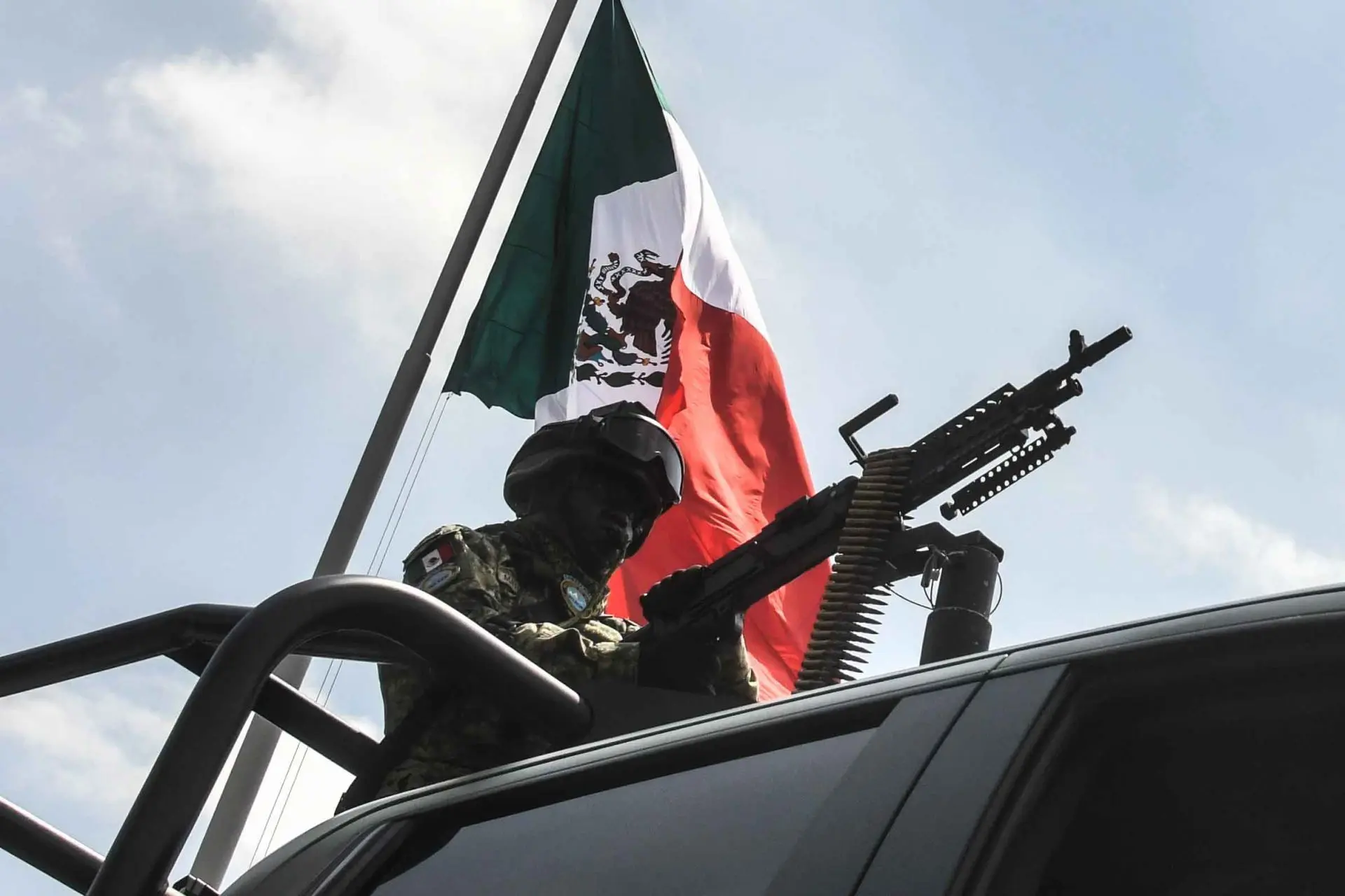 Un militar sobre una camioneta; a lo lejos, la bandera de México.<br>
