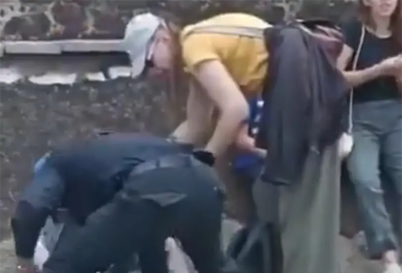 En el centro de la escena, un hombre con la pierna ensangrentada permanece recostado mientras quienes lo rodean buscan mantenerlo consciente y con vida.