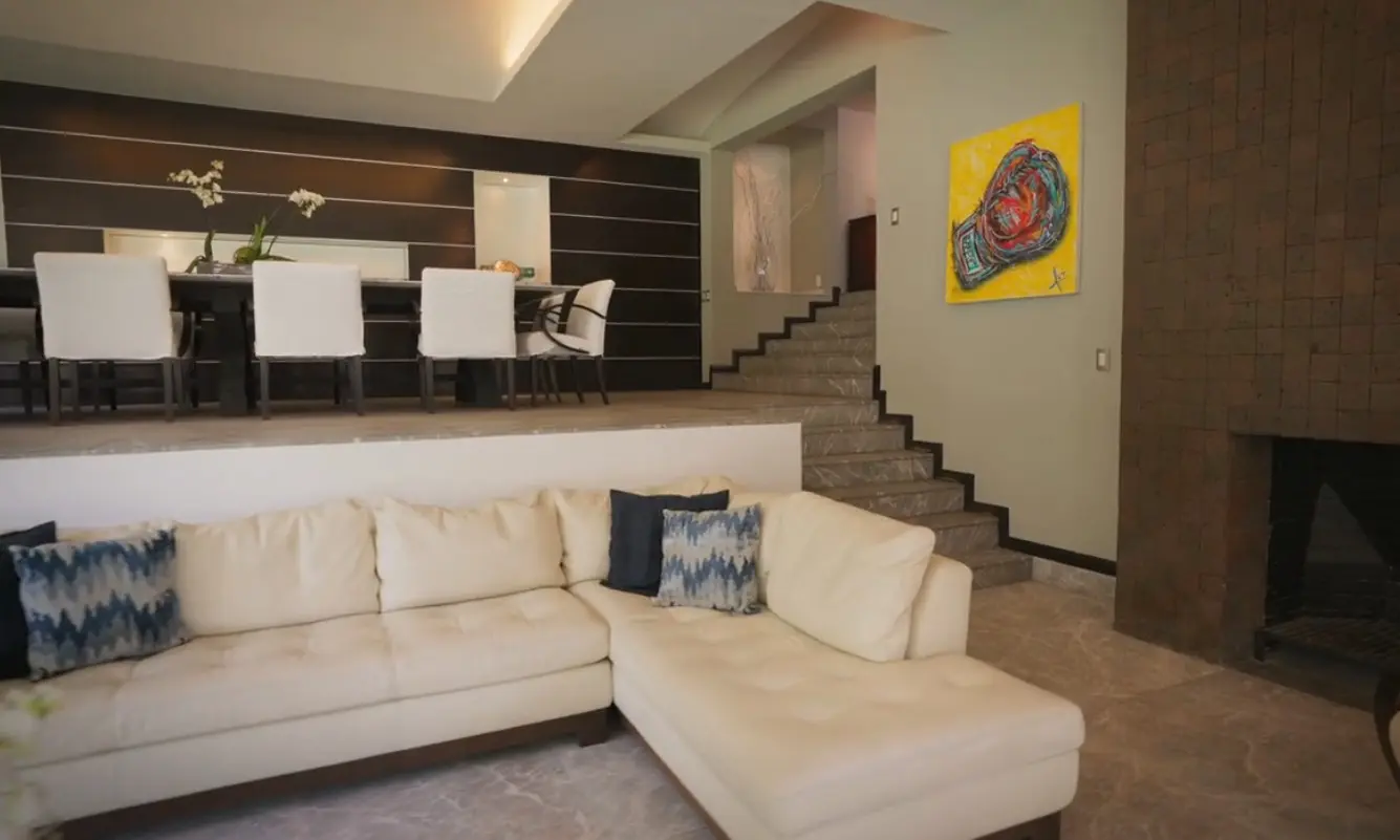 La sala principal tiene grandes sillones en tonos claros y una chimenea que aporta un ambiente acogedor.
