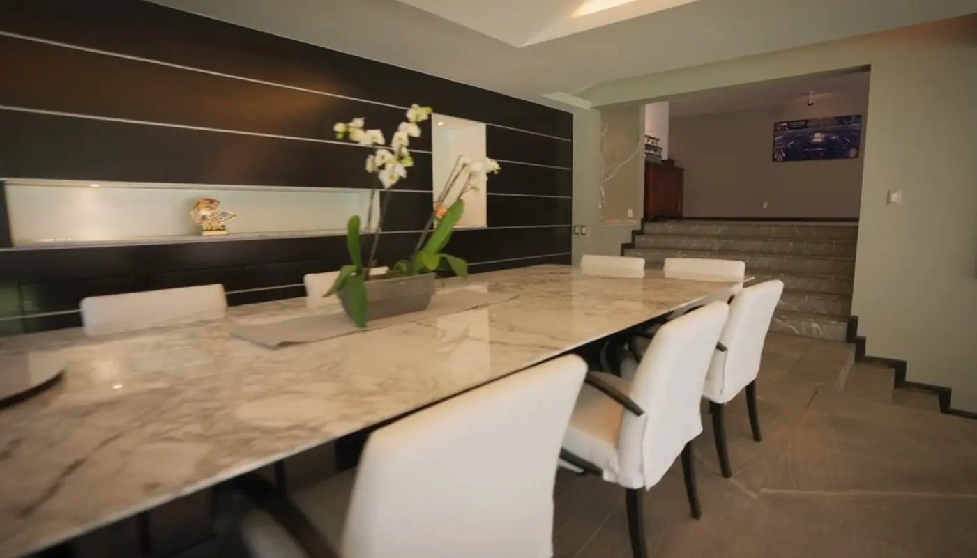 El comedor principal cuenta con una enorme mesa de m&aacute;rmol rodeada de sillas blancas y vista hacia otras &aacute;reas de la casa.